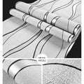 Roll of grey 3D curve stripe textured velvet wallpaper against a wall.