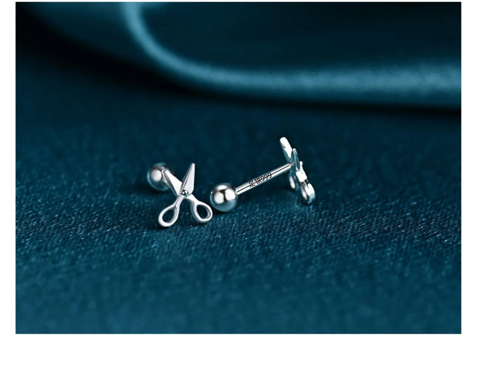 A pair of pure silver screw-style ear nails featuring a miniature scissors charm.