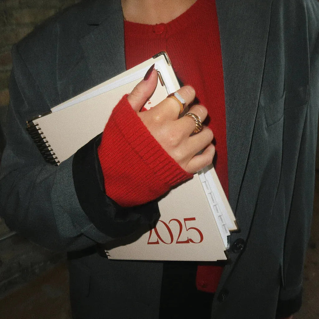 Cherry red spiral coil-bound daily schedule notebook lying open on a table.