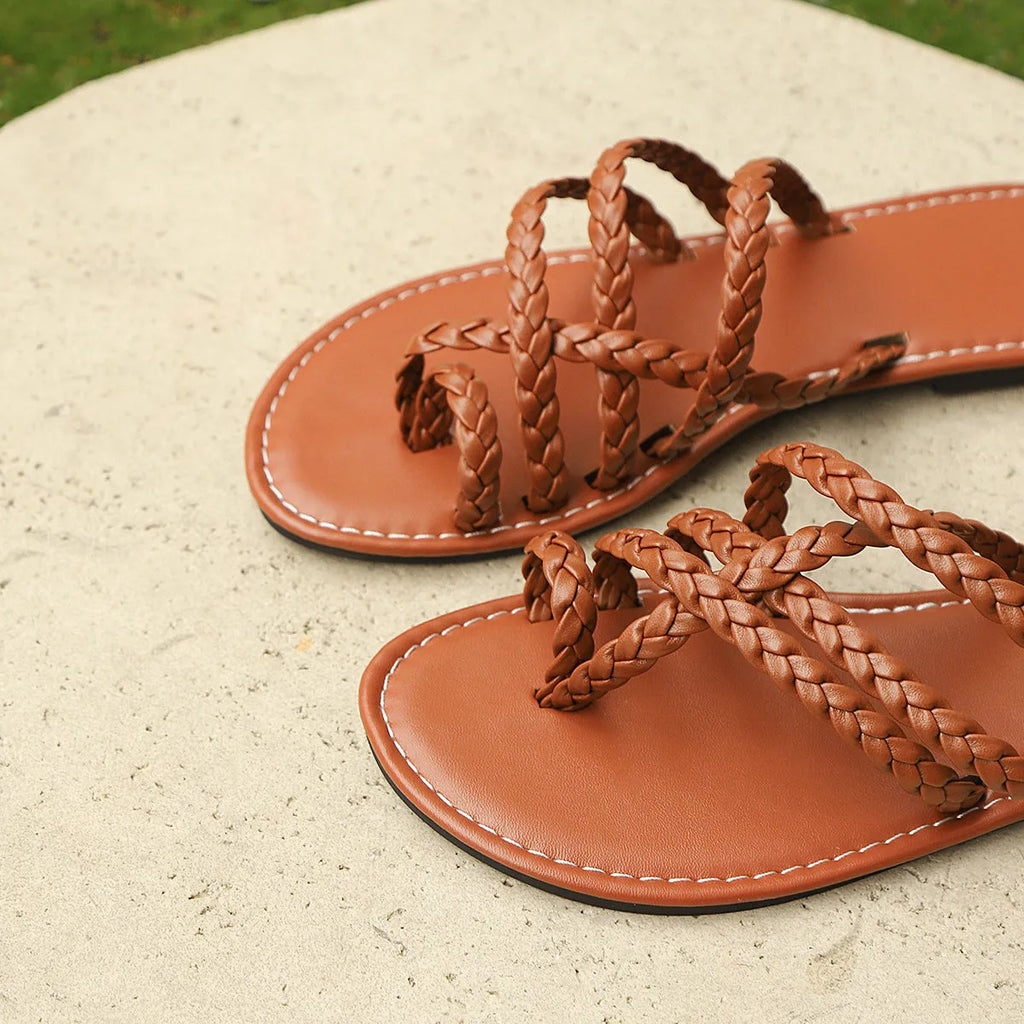 Women's white woven clip-toe flat sandals with a rubber sole on a sandy beach.