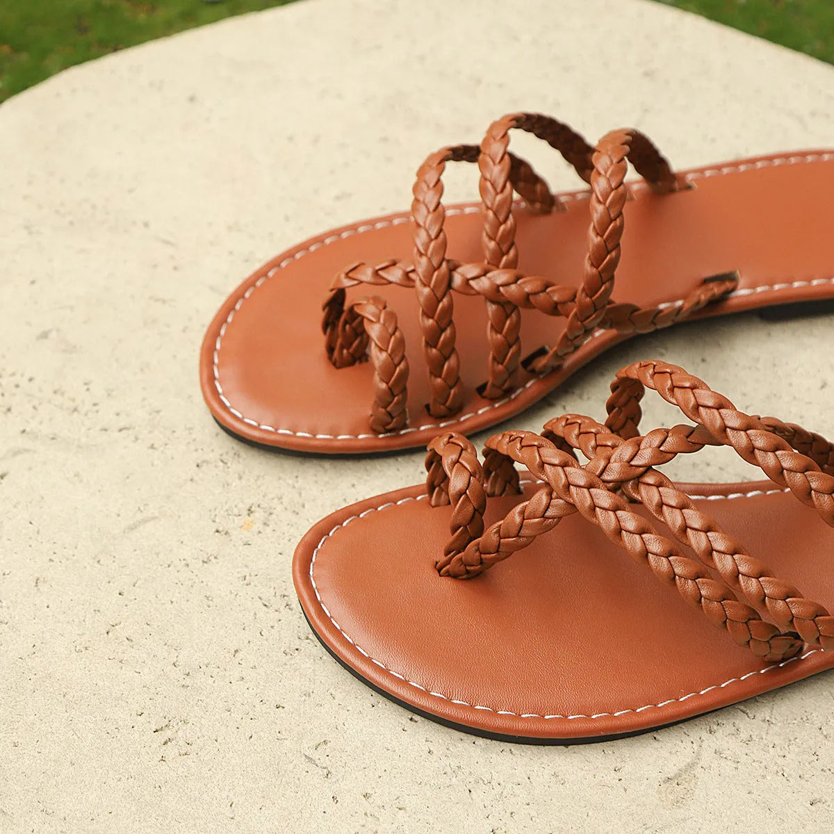 Women's white woven clip-toe flat sandals with a rubber sole on a sandy beach.