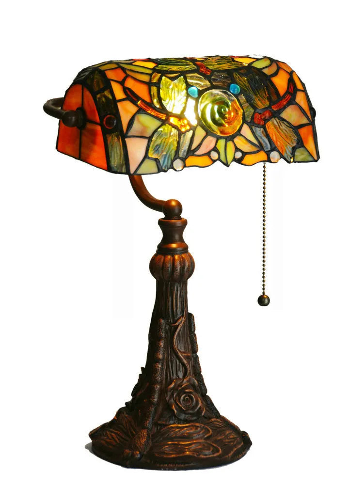 Tiffany-style table lamp with coloured glass shade and resin base on a wooden desk.