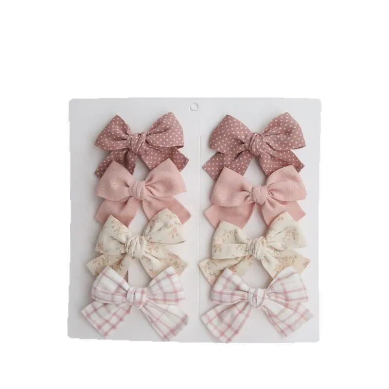 Set of eight children's cloth bow hairclips in assorted colours including beige, blue flowers, and polka dots.