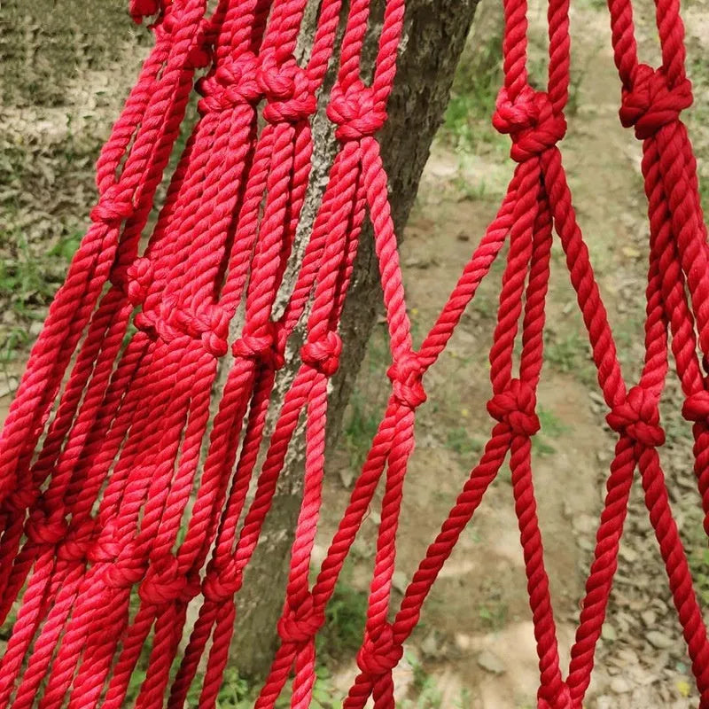 Outdoor nylon rope mesh hammock hung between two trees showing its woven construction and included tying ropes.