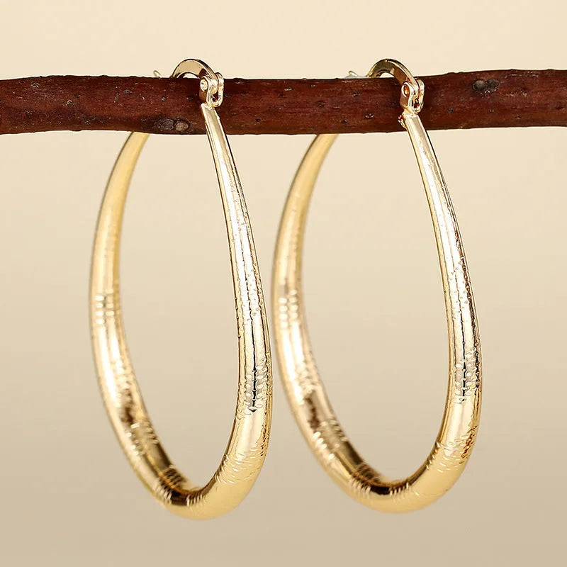 Close-up of women's geometric drop-shaped clip-on earrings with ring and line design in a copper and electroplated finish.