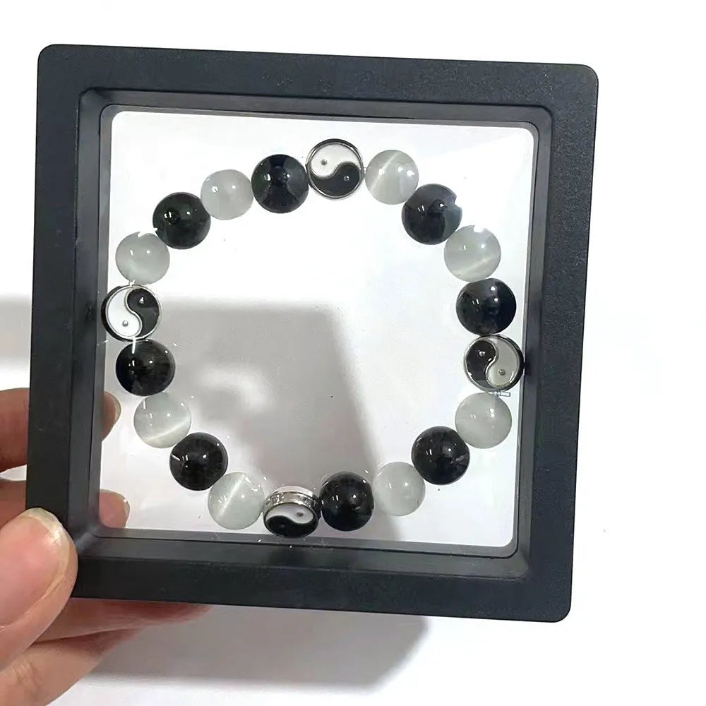 A polished black agate opal beaded bracelet with an ornamental Tai Chi symbol, shown on a wrist.