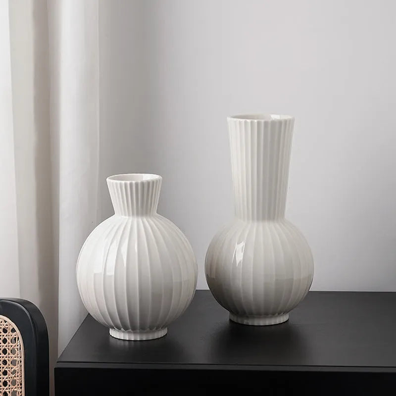 White ceramic ball vase with vertical stripes on a wooden table, with optional artificial purple orchid stems.