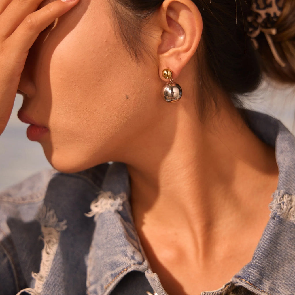 Pair of round bead stud earrings with gold plating and colour-block design on a woman's earlobe.