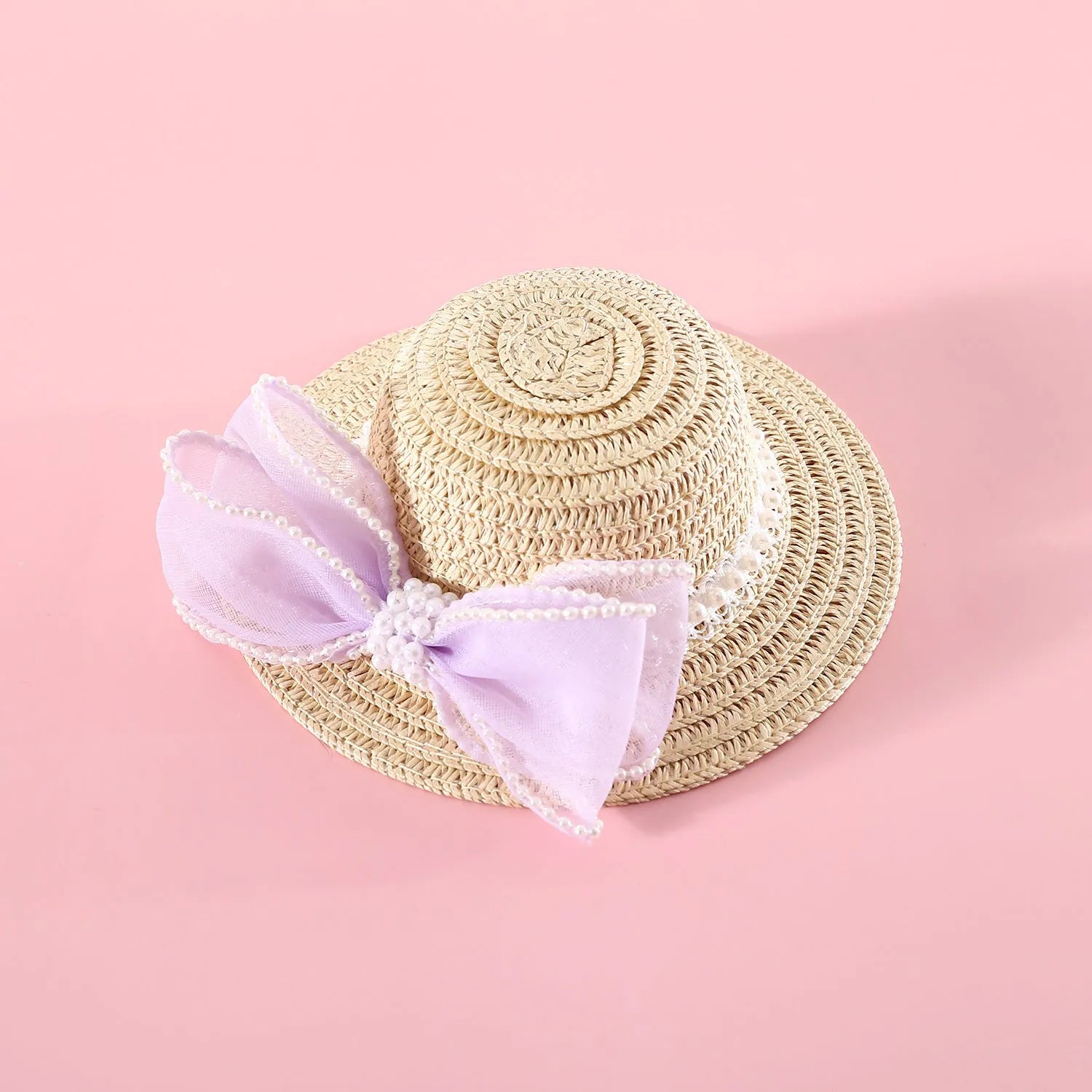 Cat wearing a woven straw hat with a pearl butterfly bow on its head.