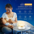 White cylindrical bedside night light with touch controls on a wooden surface.