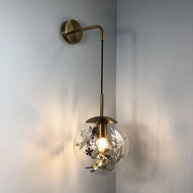 Modern glass wall lamp in golden flower finish mounted beside a bed.