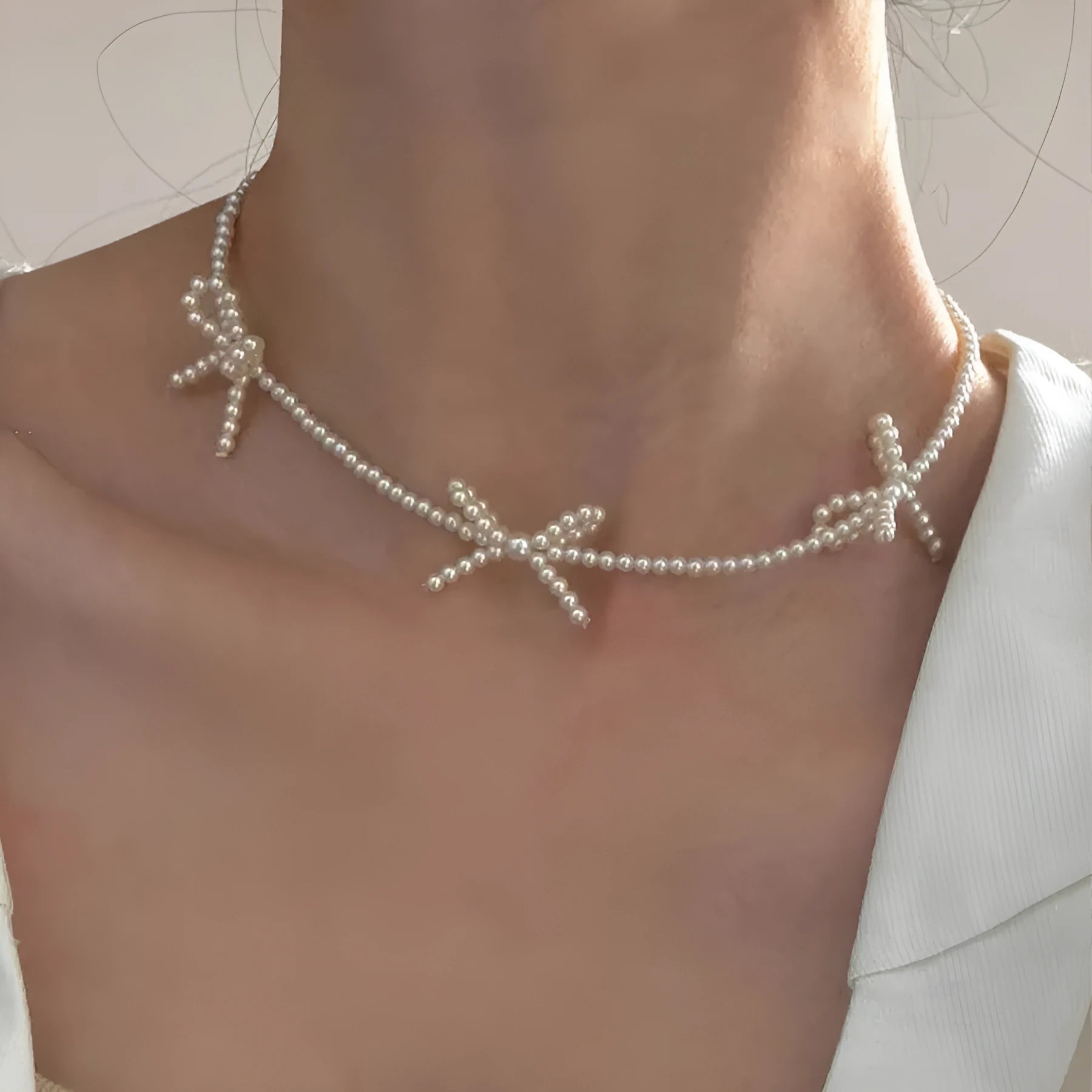 White imitation pearl necklace with a geometric bow charm on an adjustable chain.