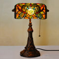 Tiffany-style table lamp with coloured glass shade and resin base on a wooden desk.