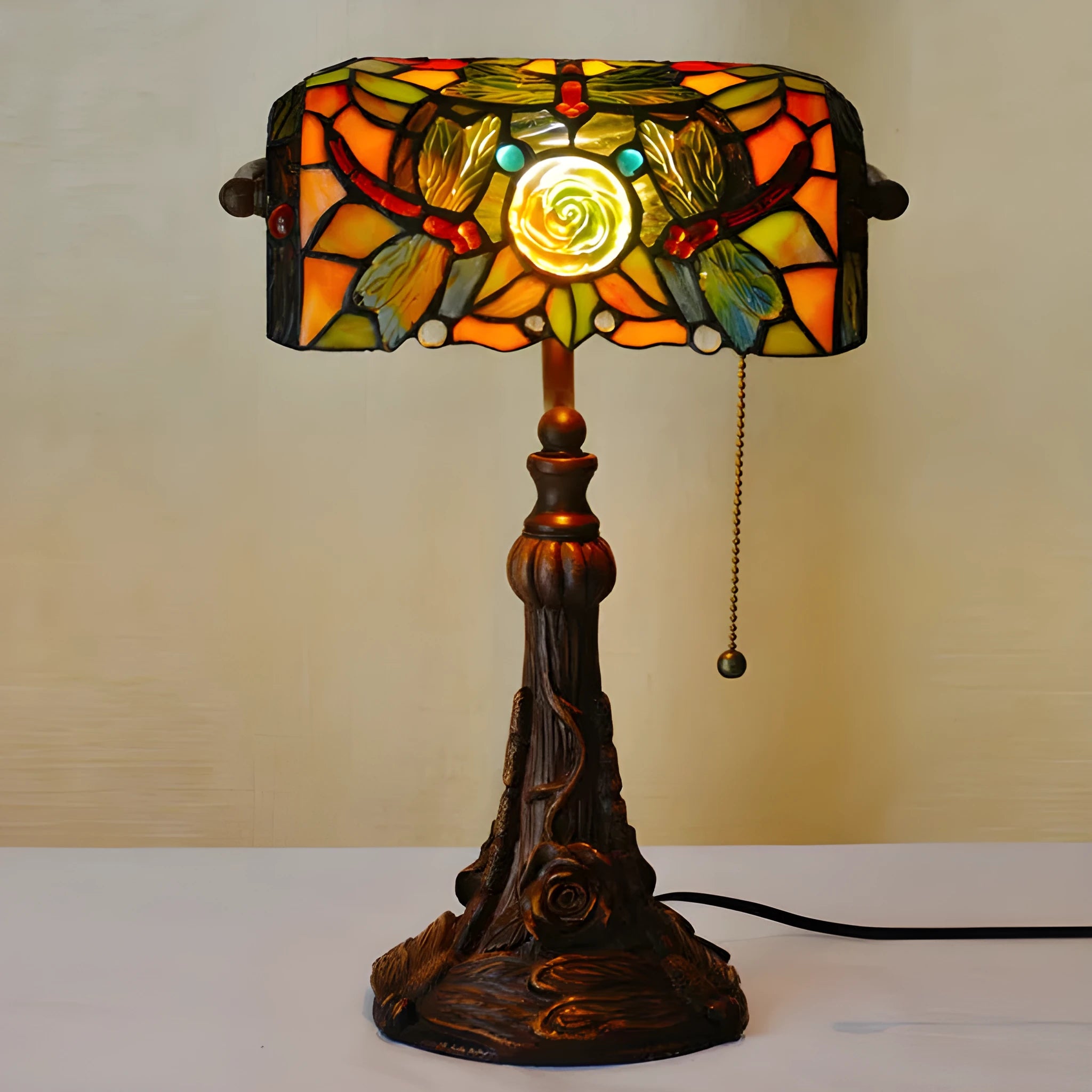 Tiffany-style table lamp with coloured glass shade and resin base on a wooden desk.