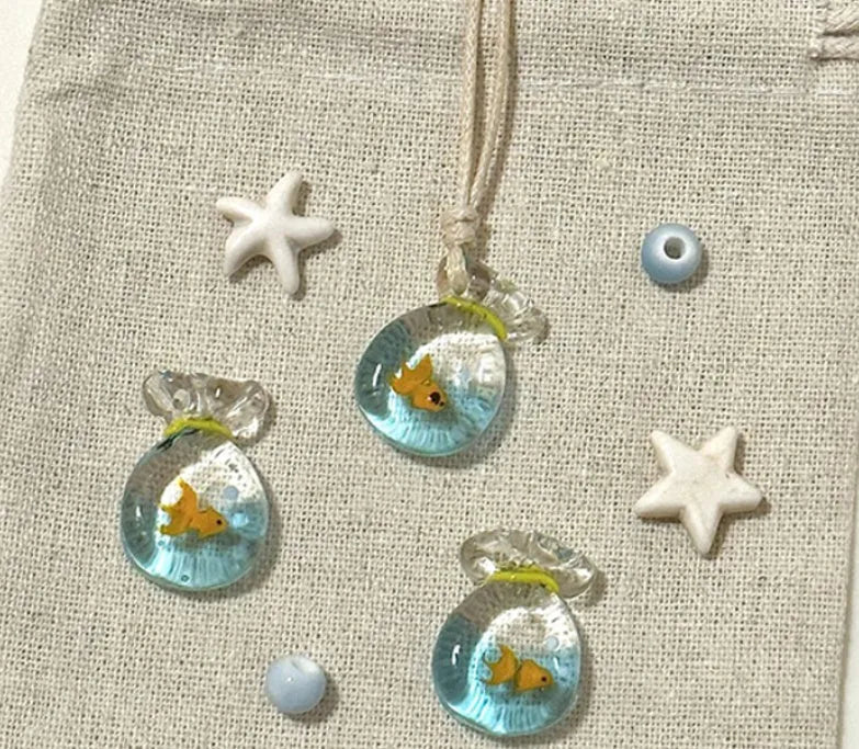 Women's necklace with blue glazed small fish charm pendant on a beige cotton-linen clavicle chain.