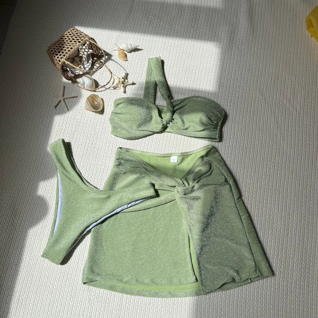 Women's light green one-shoulder tube top swimsuit set with matching shorts and wrap skirt.