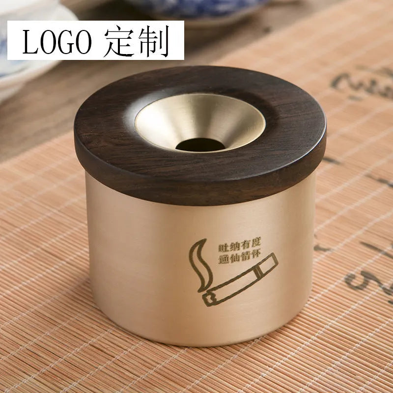 Brass-coloured copper ashtray with a wooden lid featuring a central hole, on a tabletop.