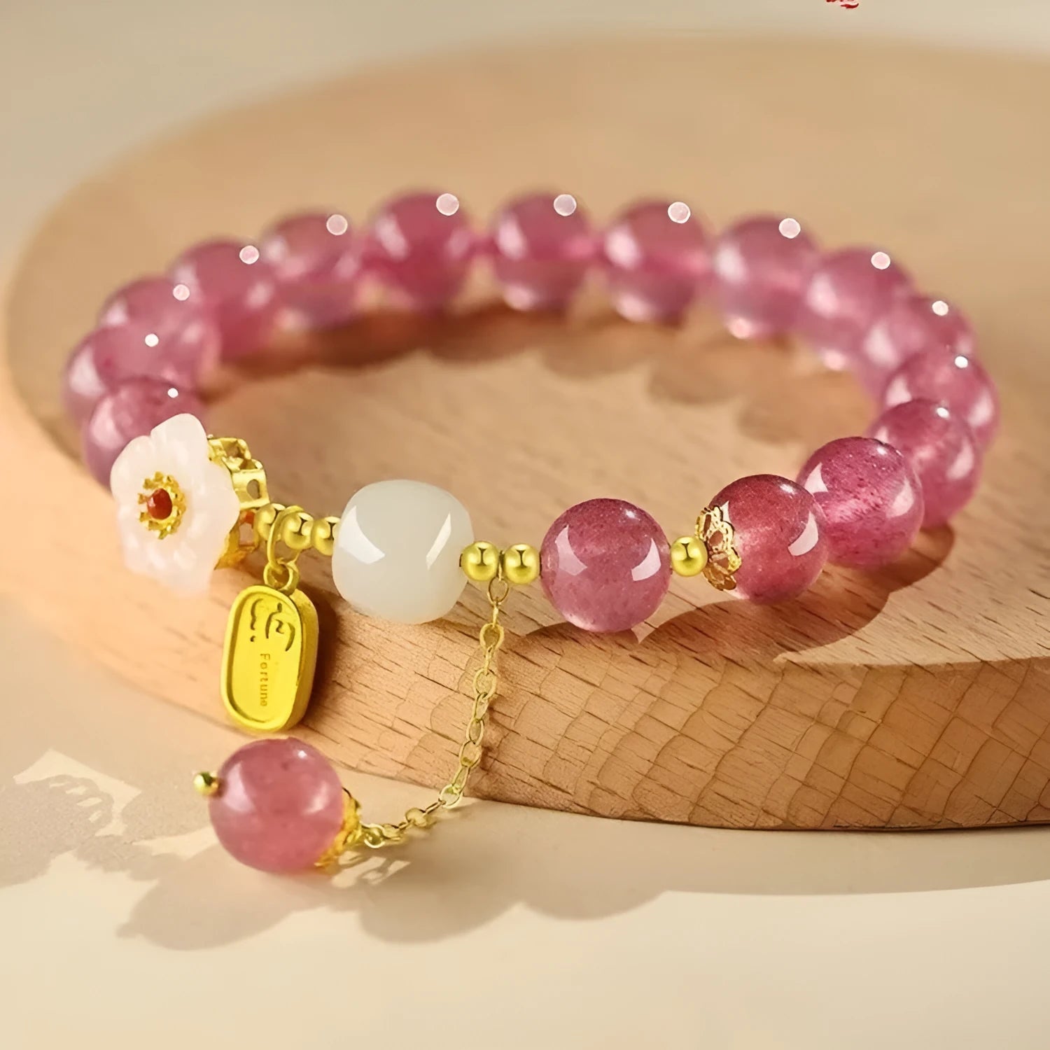 Handmade strawberry quartz crystal bracelet with peach blossom charms on a wrist.