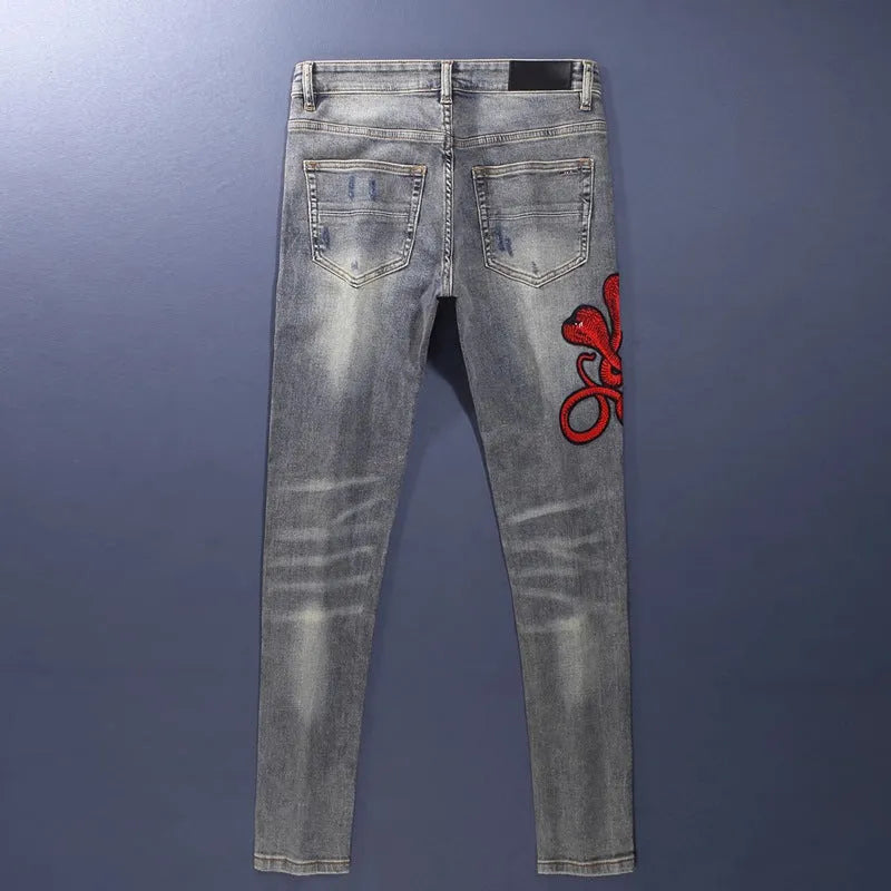 Slim fit light blue jeans with worn patches and embroidery on the legs, showing a washed-out colour.