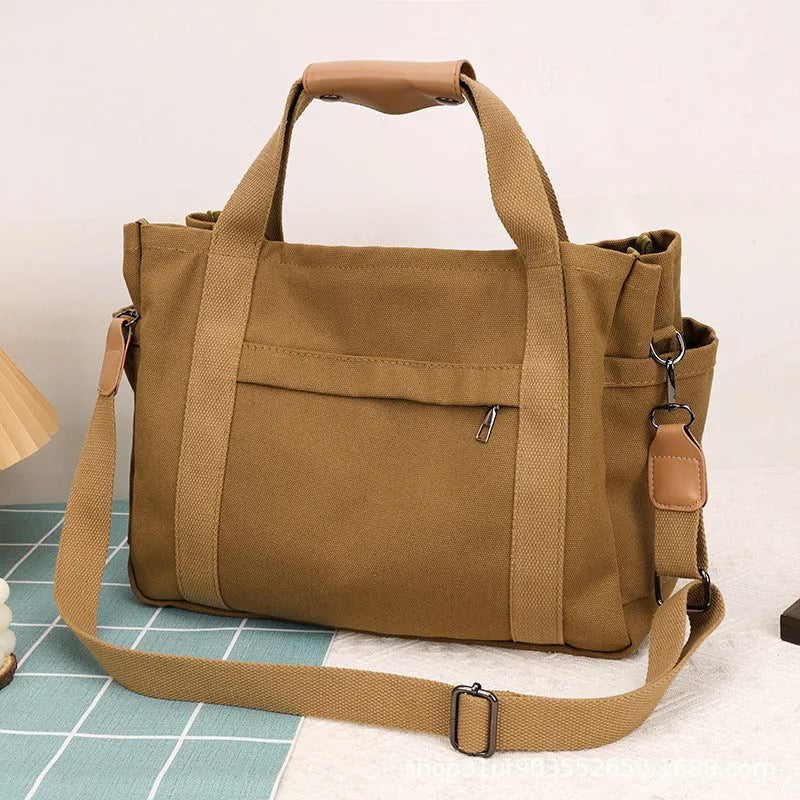 Army green canvas tote bag with open zip sides showing internal laptop and camera pockets.