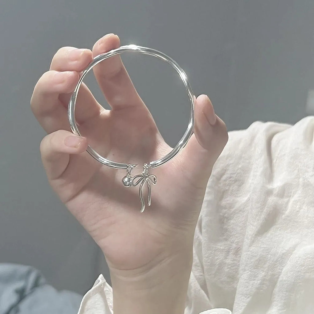 Silver adjustable women's bracelet with a bow bell charm on a zinc alloy bangle.