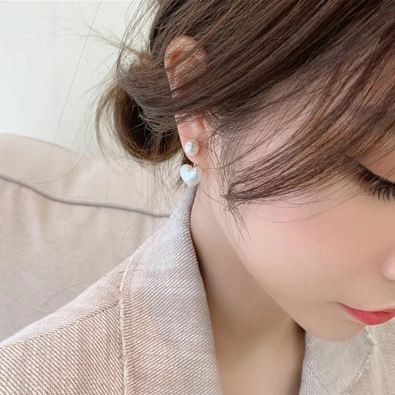Close-up of women's simple heart-shaped stud earrings with a pearl-like finish and Korean style design.