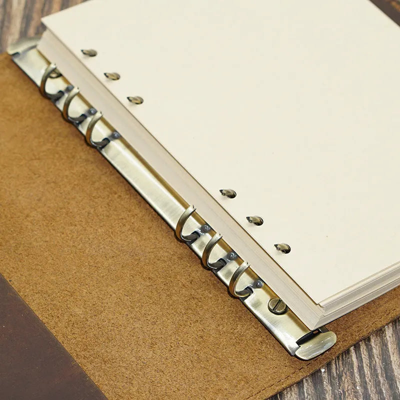 A5 handmade cowhide leather loose-leaf notebook in black with 100 sheets of kraft paper on a desk