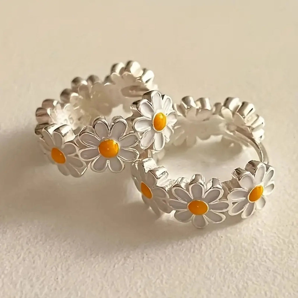 A pair of white daisy flower ring earrings with a gemstone inlay, shown on a model or display.