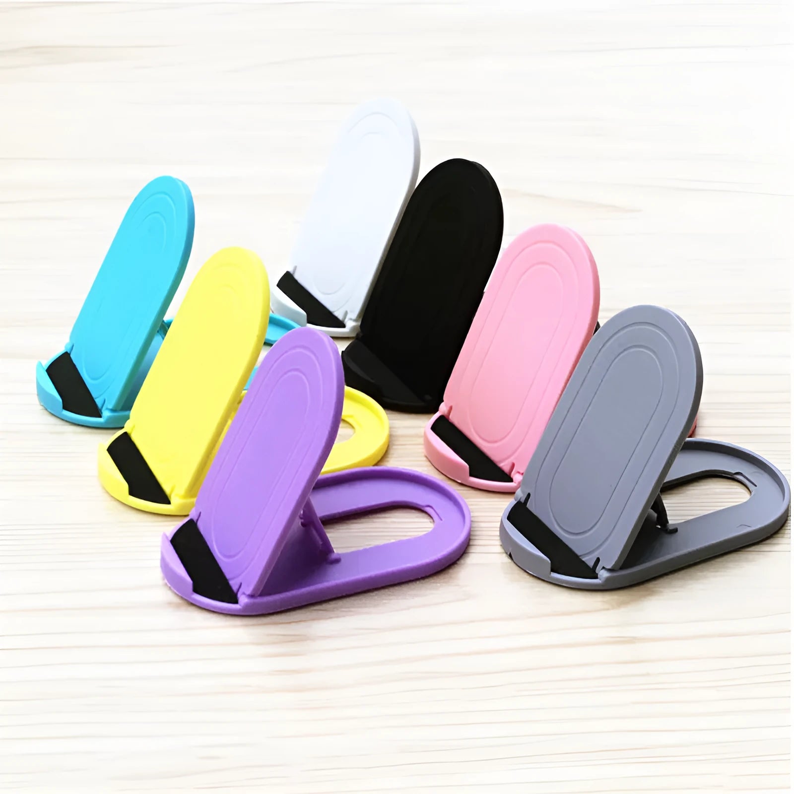 A plastic lazy bracket mobile phone stand on a table, shown in one of six available colours.