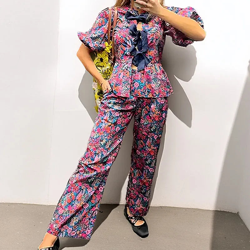 Women's floral print two-piece trouser suit with puff sleeve top and matching trousers.