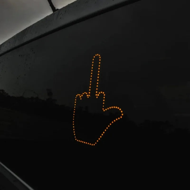 Black plastic LED car gesture light showing illuminated middle finger sign on dashboard