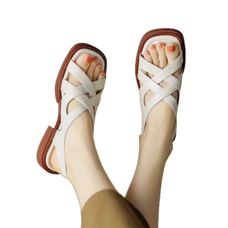 Glossy black patent leather women's sandals with a square toe and ankle strap on a flat rubber sole.