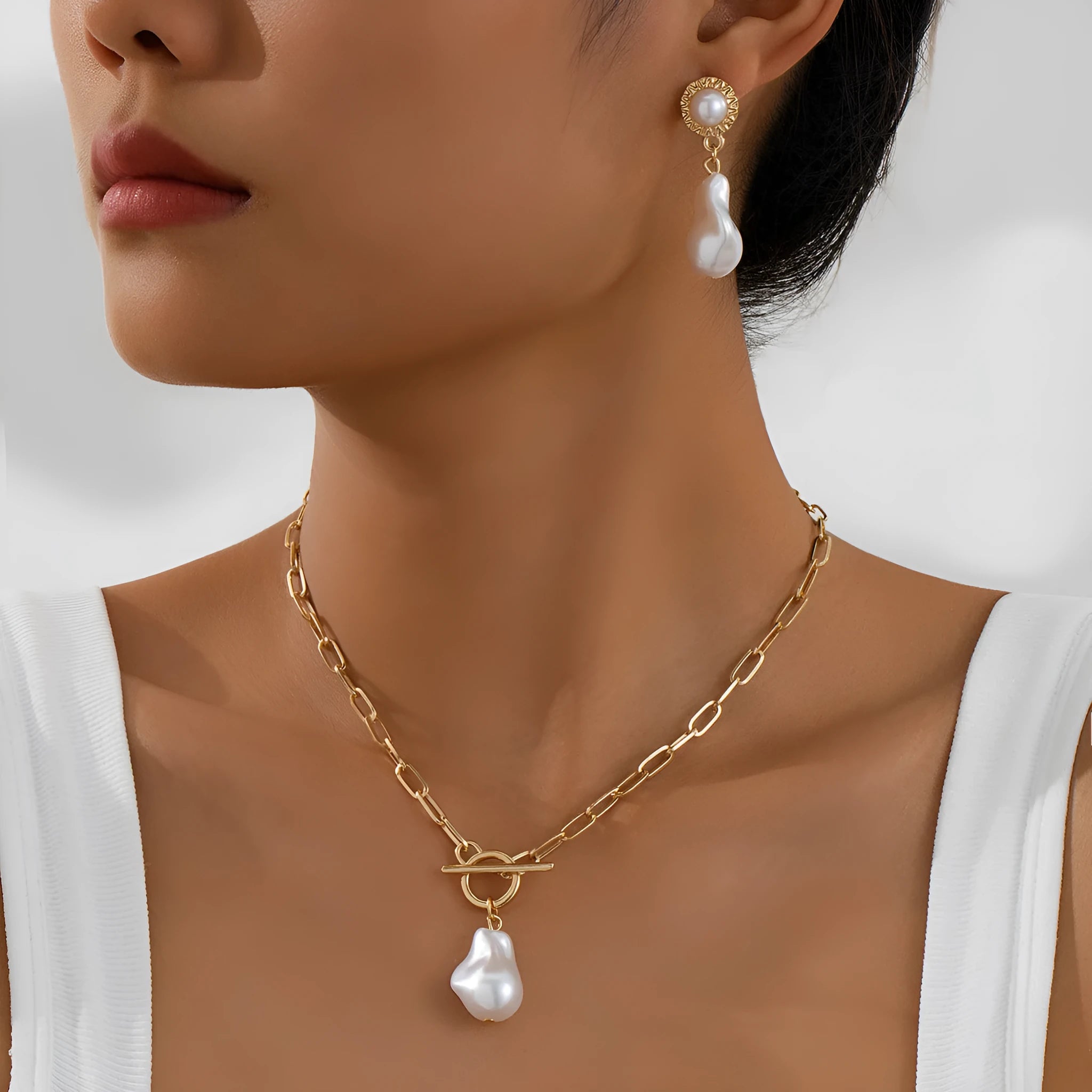 Gold baroque pearl pendant necklace and ear stud set for women on a white background.