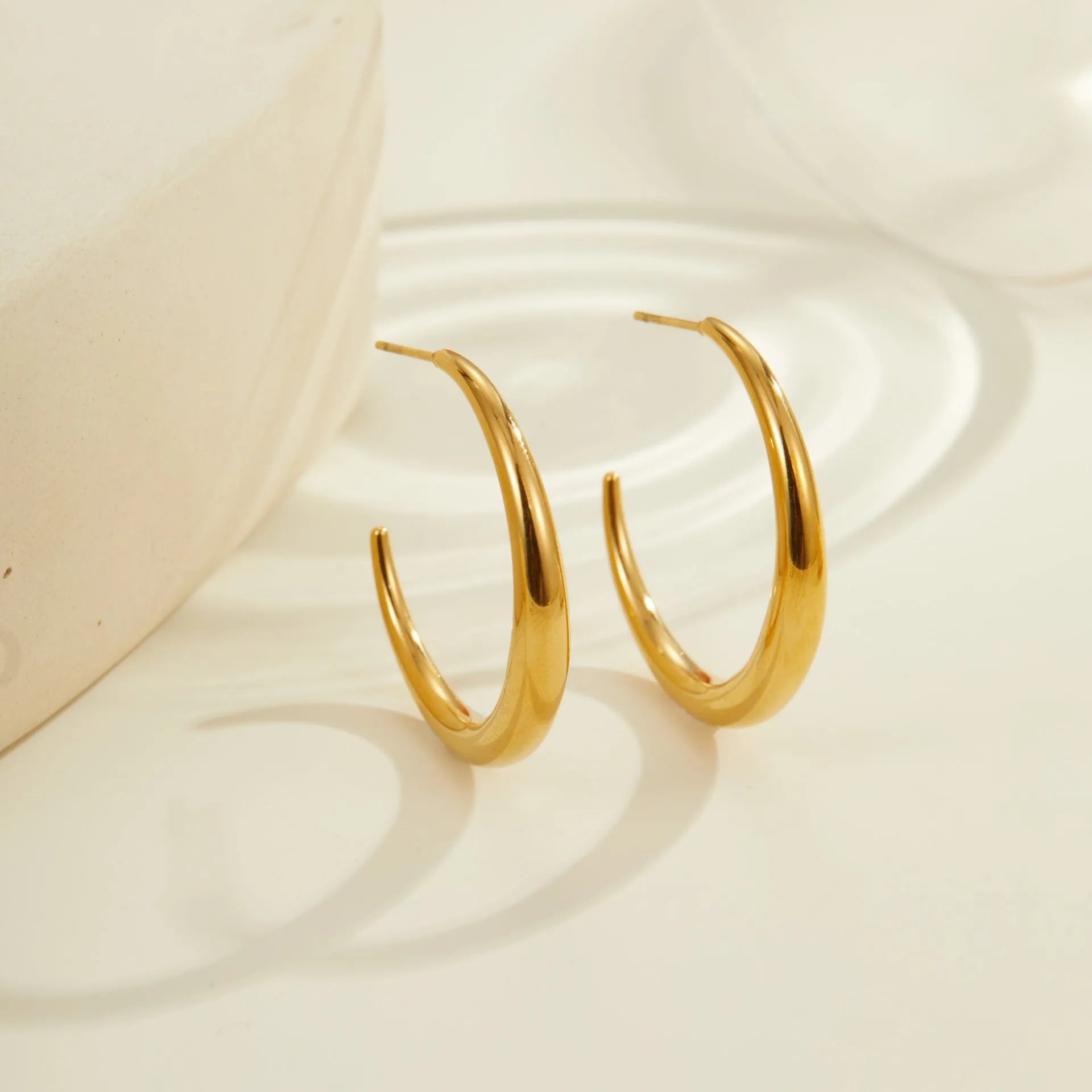 A pair of simple round titanium steel hoop earrings for women, shown in gold and steel finishes.