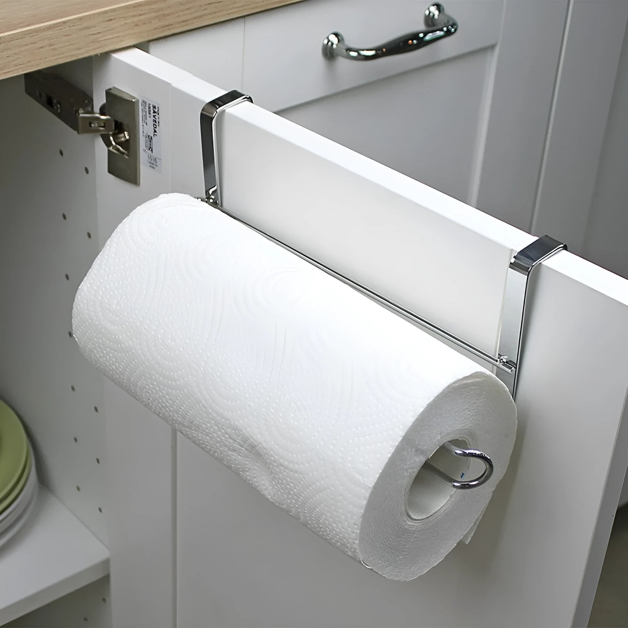 Silver stainless steel paper towel rack hanging on a kitchen cabinet door.