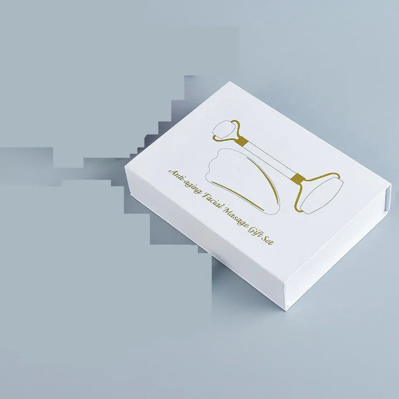White jade facial roller and gua sha scraping tool set on a storage board.