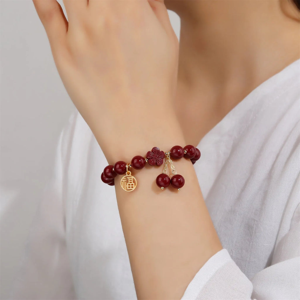 Women's handmade cinnabar bracelet with fu character charm and tassel detail in purple gold sand finish