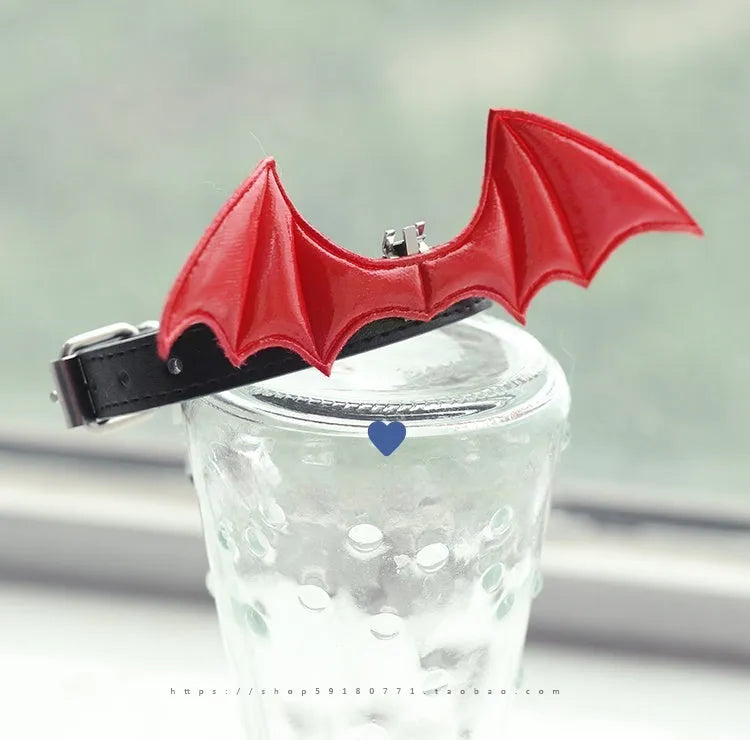 Black patent leather dog collar with small devil wings and a bell attached.