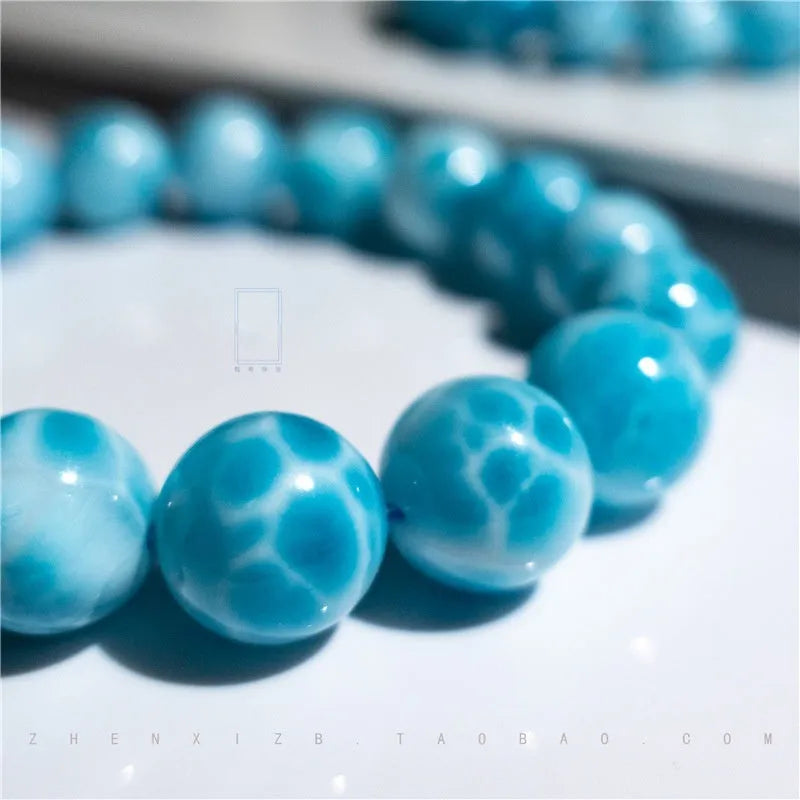 Blue handcrafted bodhi bracelet with sea-pattern crystal stones and pearl accents on a neutral background.