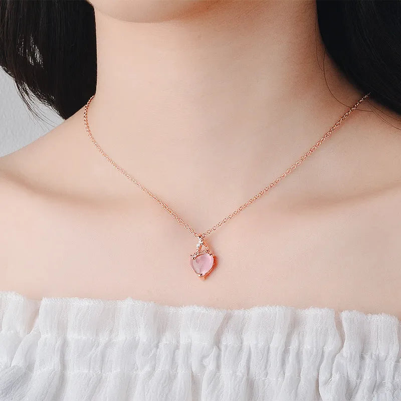 Women's pink heart crystal pendant necklace with rose gold cross chain on copper.