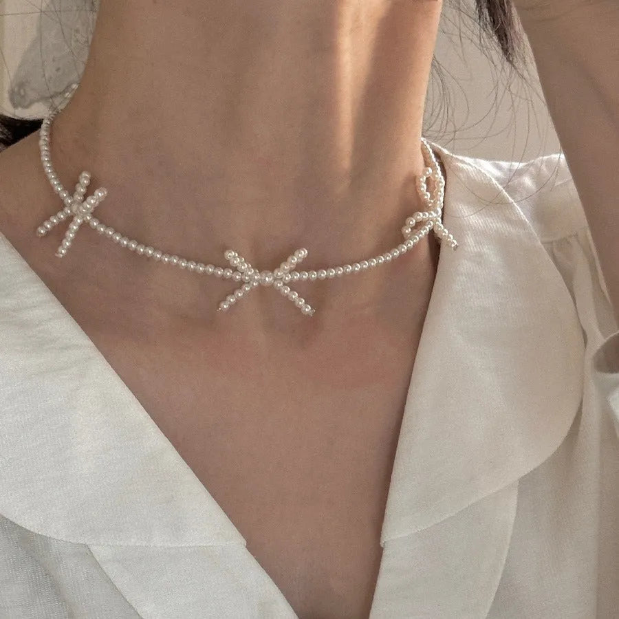 White imitation pearl necklace with a geometric bow charm on an adjustable chain.
