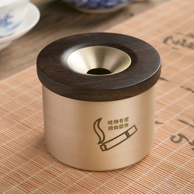 Brass-coloured copper ashtray with a wooden lid featuring a central hole, on a tabletop.