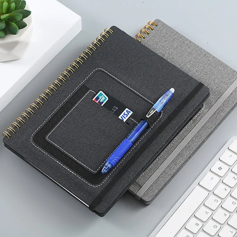 Erasable coil-bound notebook with stone paper, shown with pen and cloth on a wooden desk.