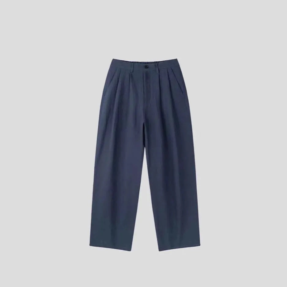 Men's apricot coloured loose-fit cotton linen trousers with a pencil leg and elastic waist on a neutral background.