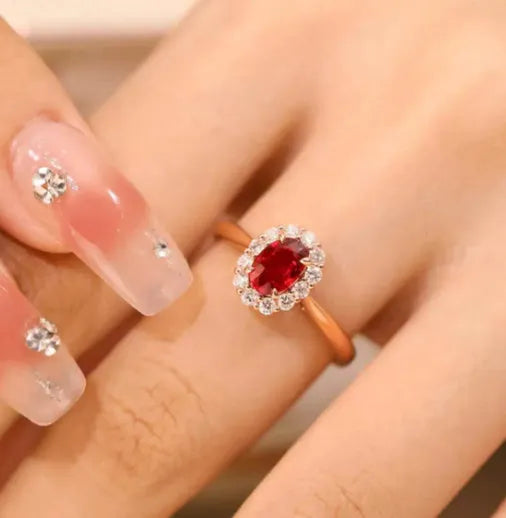 Women's silver ring with gold pigeon and red gemstone floral inlay on a finger.