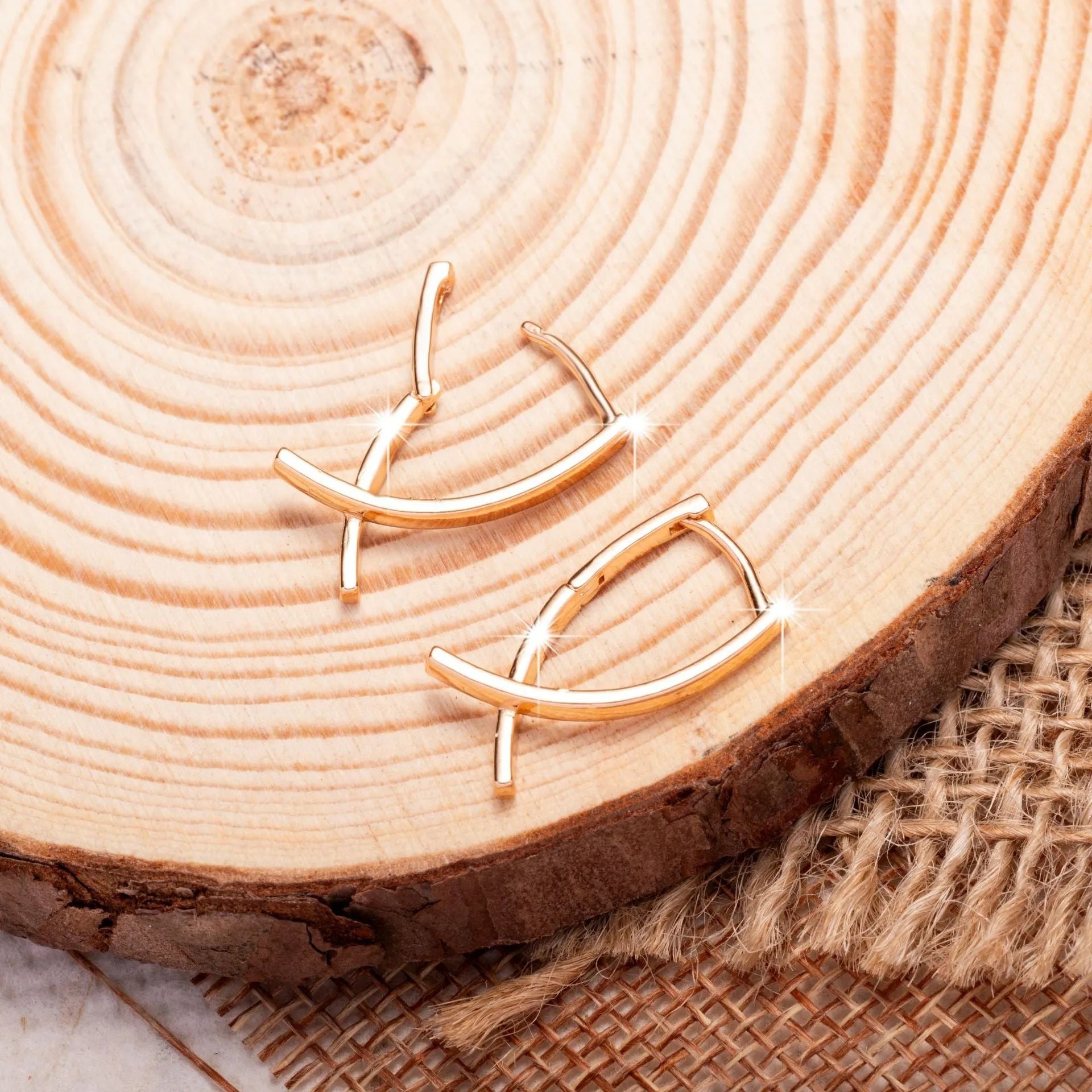 A pair of rose gold cross shaped earrings made from copper on a plain background.
