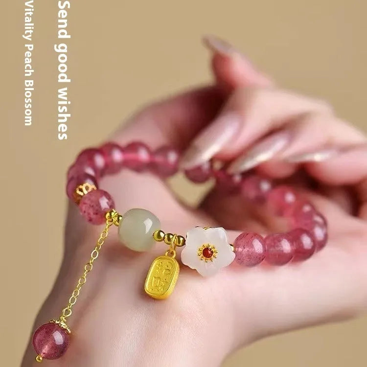 Handmade strawberry quartz crystal bracelet with peach blossom charms on a wrist.