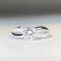 Geometric silver ring with twisted band and a 1 karat moissanite stone in a four-claw setting.