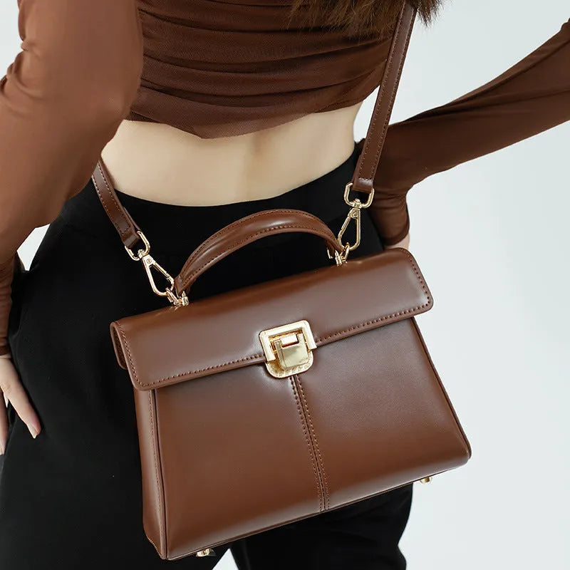 Black leather women's shoulder bag with vachette clasp showing horizontal square shape and adjustable strap