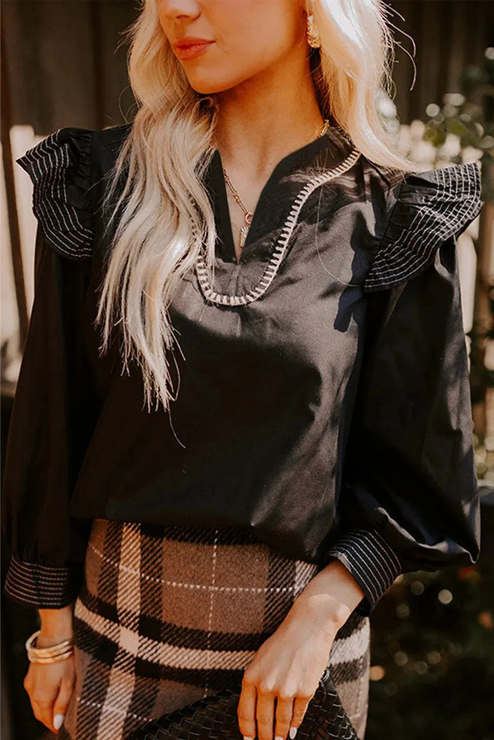 Black women's V-neck blouse with contrast stitching and ruffle detail on long sleeves